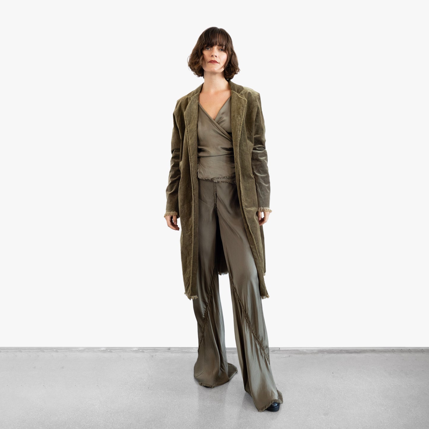 Model wearing a green velvet coat over a green silk wrap top and pants