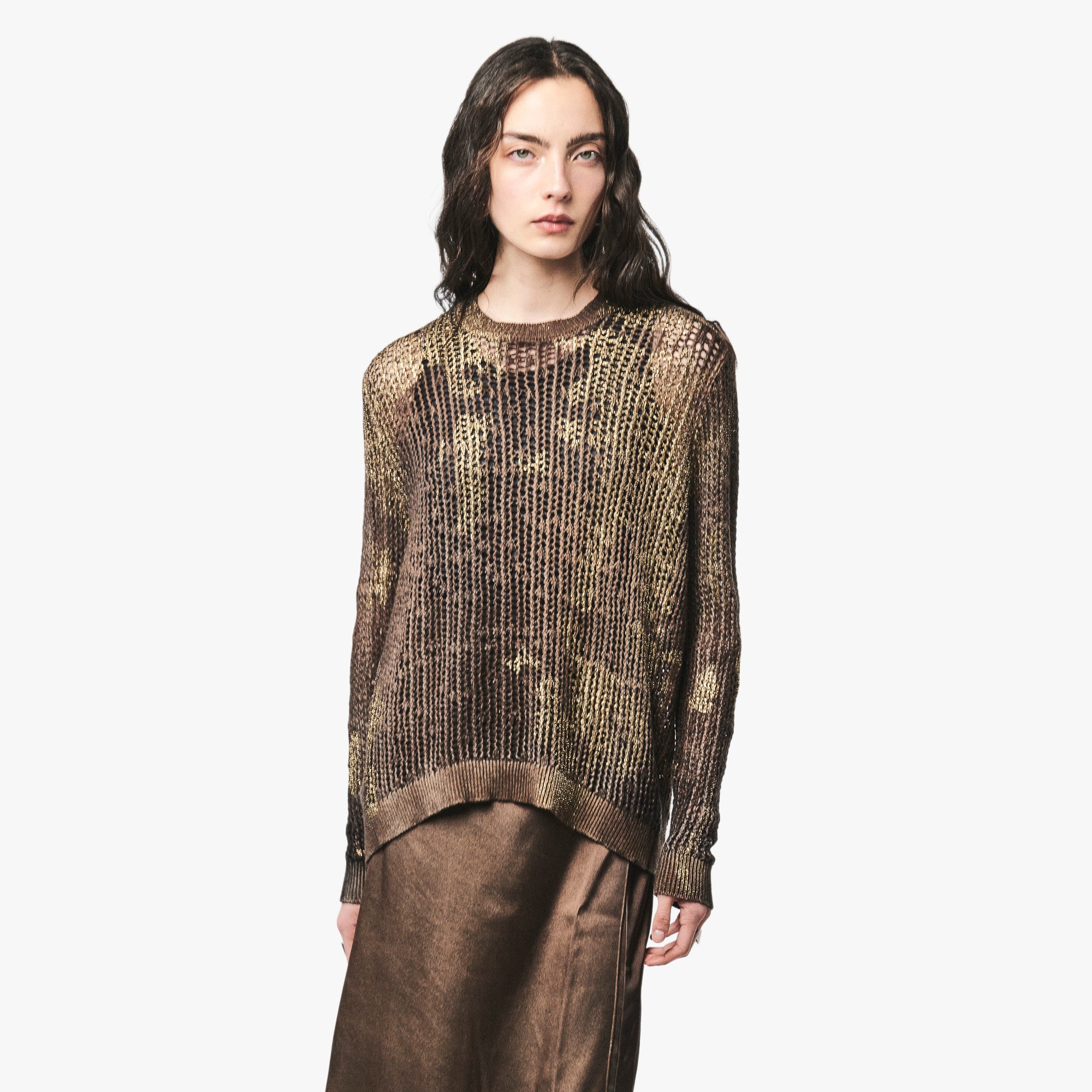 A model wearing a metallic bronze and gold textured knit sweater, paired with a brown skirt, against a solid light gray background.