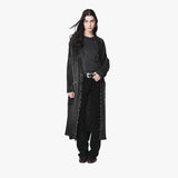 A model wearing a long, dark gray textured knit cardigan with fringe details over a black top and black pants, standing against a solid off-white background.