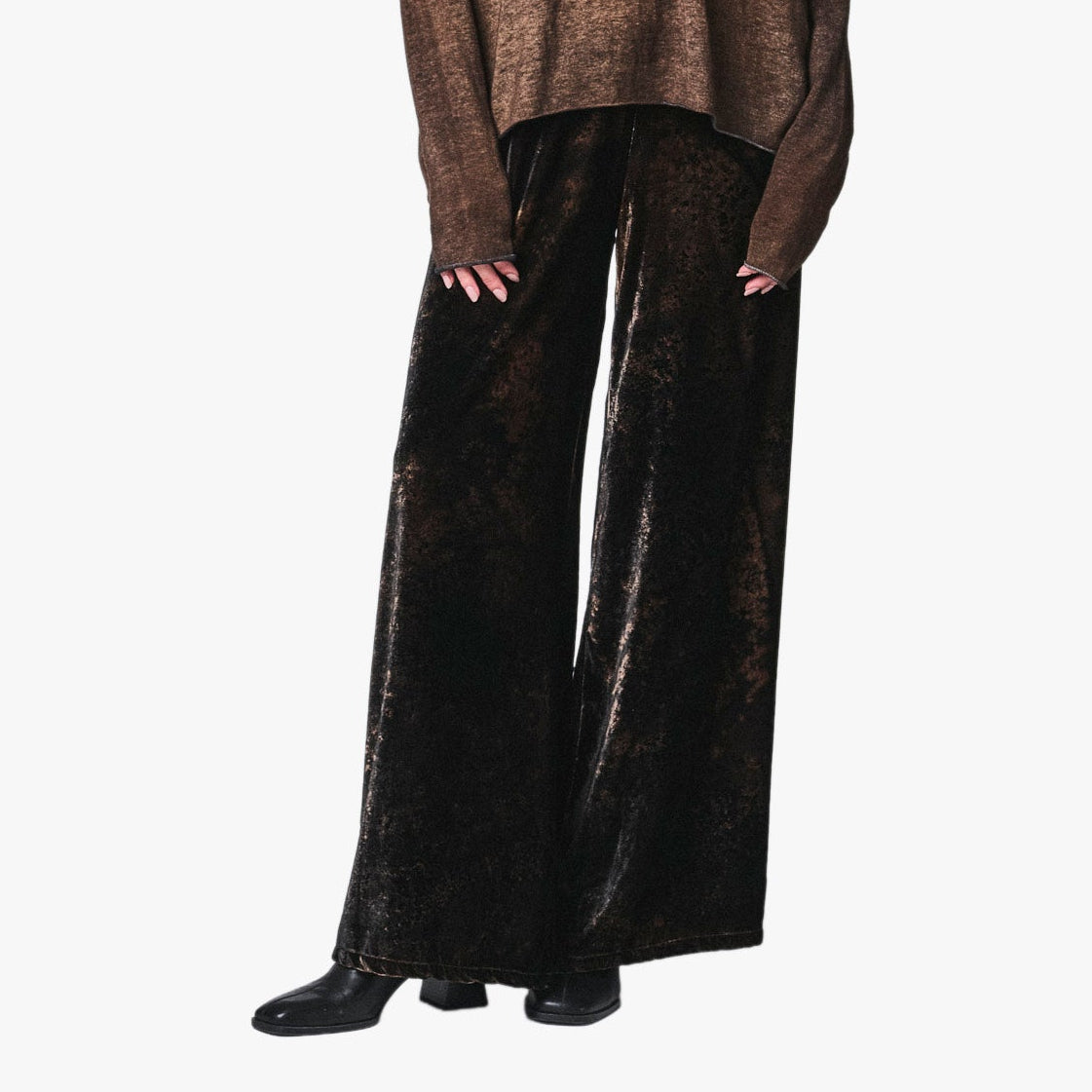 A model stands against a light gray background wearing a brown textured sweater and wide-leg velvet pants.