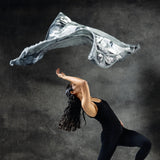 A woman dancing with a limited edition hand-painted cashmere and silk scarf in gray, black, and white tones with frayed edges and a silver lamination.