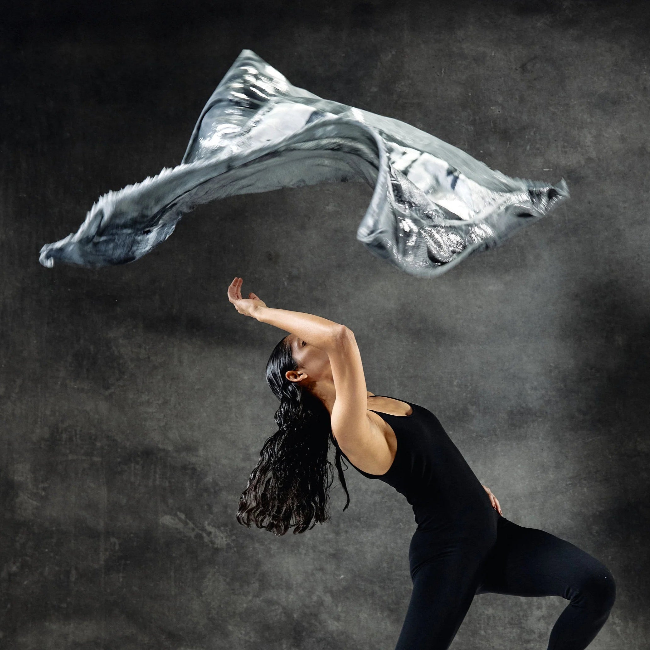 A woman dancing with a limited edition hand-painted cashmere and silk scarf in gray, black, and white tones with frayed edges and a silver lamination.