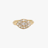A gold eye-shaped ring featuring a central round diamond surrounded by a halo of smaller diamonds, set on a plain light gray background.
