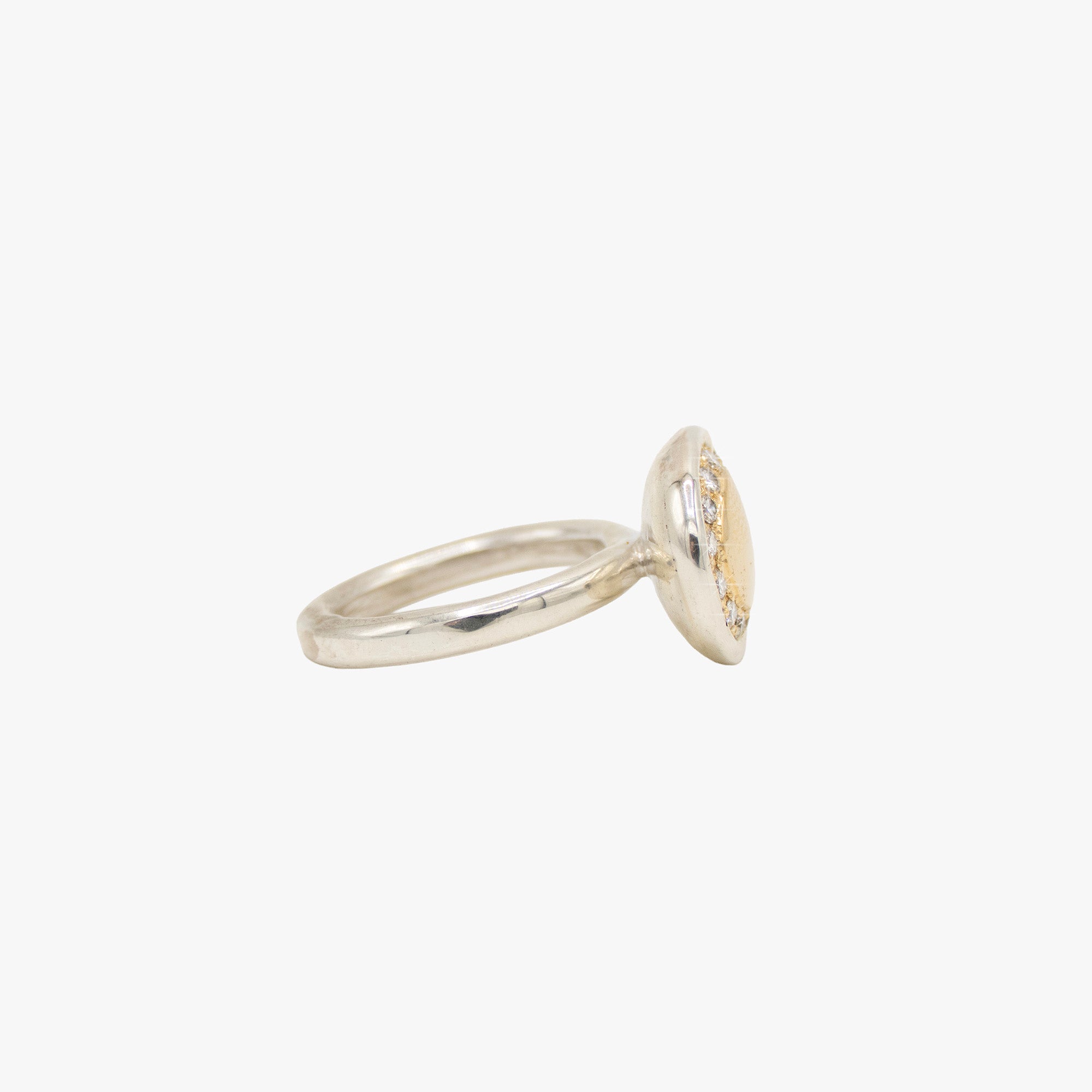 A two-tone oval ring featuring a smooth gold center surrounded by a halo of small clear stones, set in a silver-toned band.