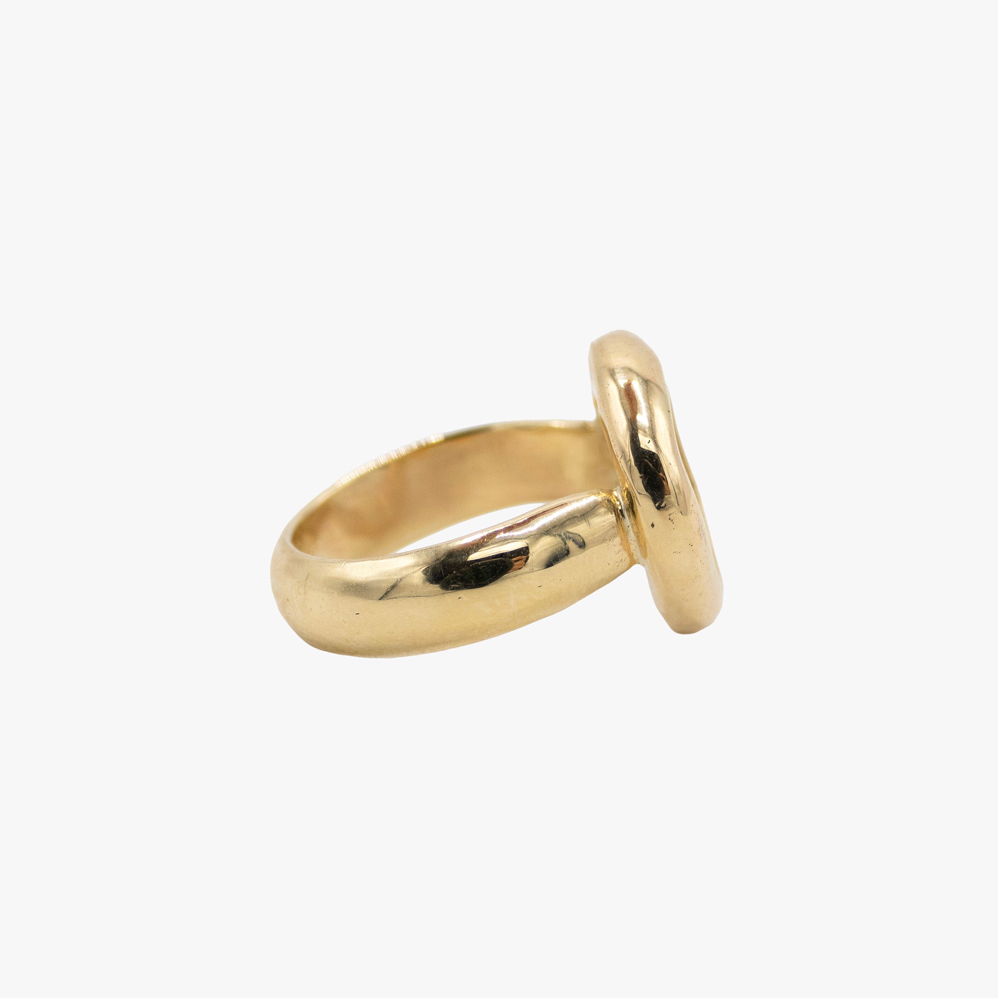 A gold ring with a thick, polished band and a round face, shown from a side angle.