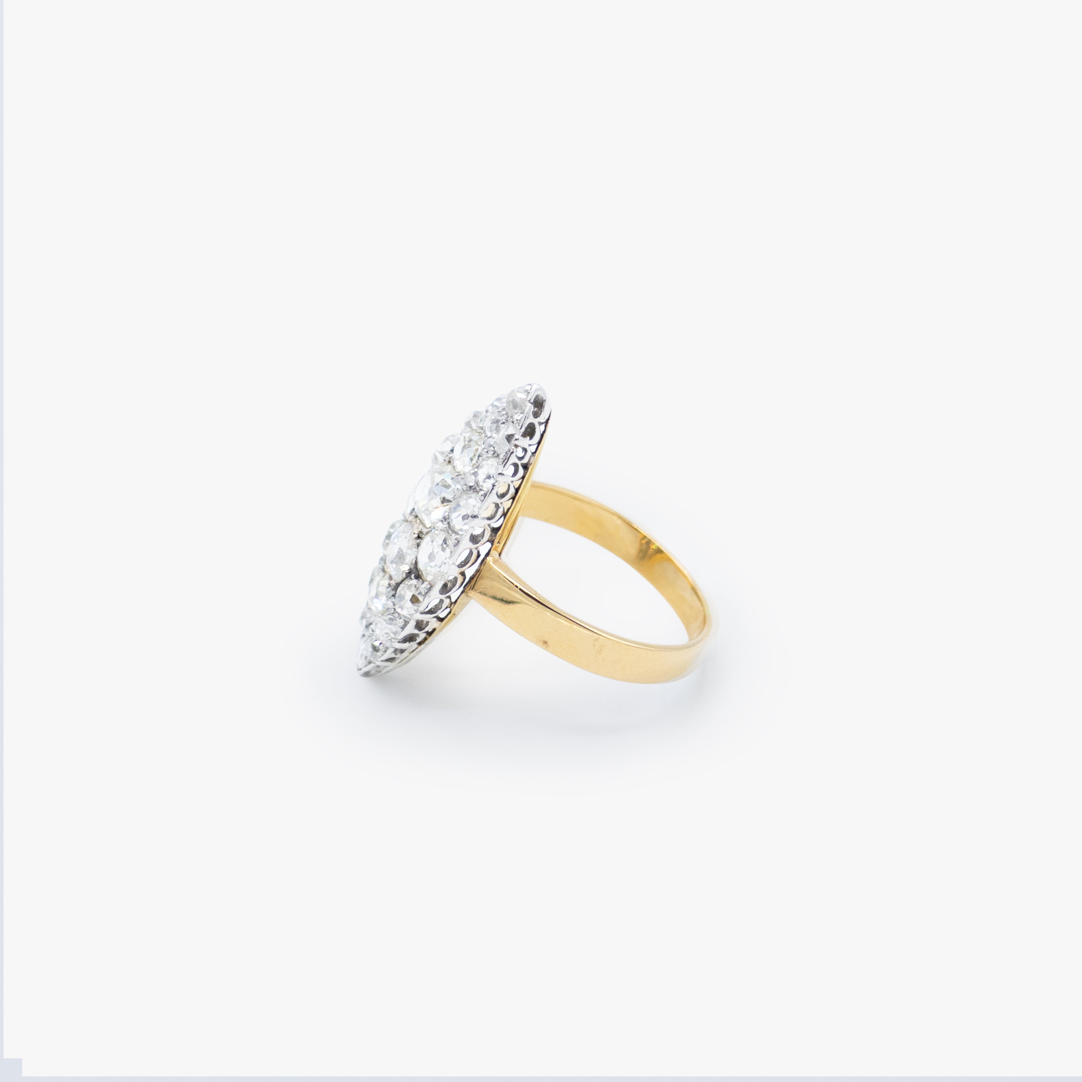 A yellow gold ring with a silver-toned oval pavé setting featuring clear round stones, shown on a light gray background.