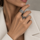 A close-up lifestyle shot of a model wearing two rings: a multi diamond band ring on the index finger and a sterling silver branch shaped ring with diamonds on the middle finger, styled with a cream-colored blazer.