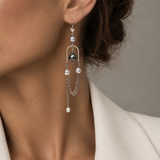 A close-up of a model wearing a long silver dangle earring with South Sea pearls and a Tahitian pearl, paired with a cream-colored blazer.