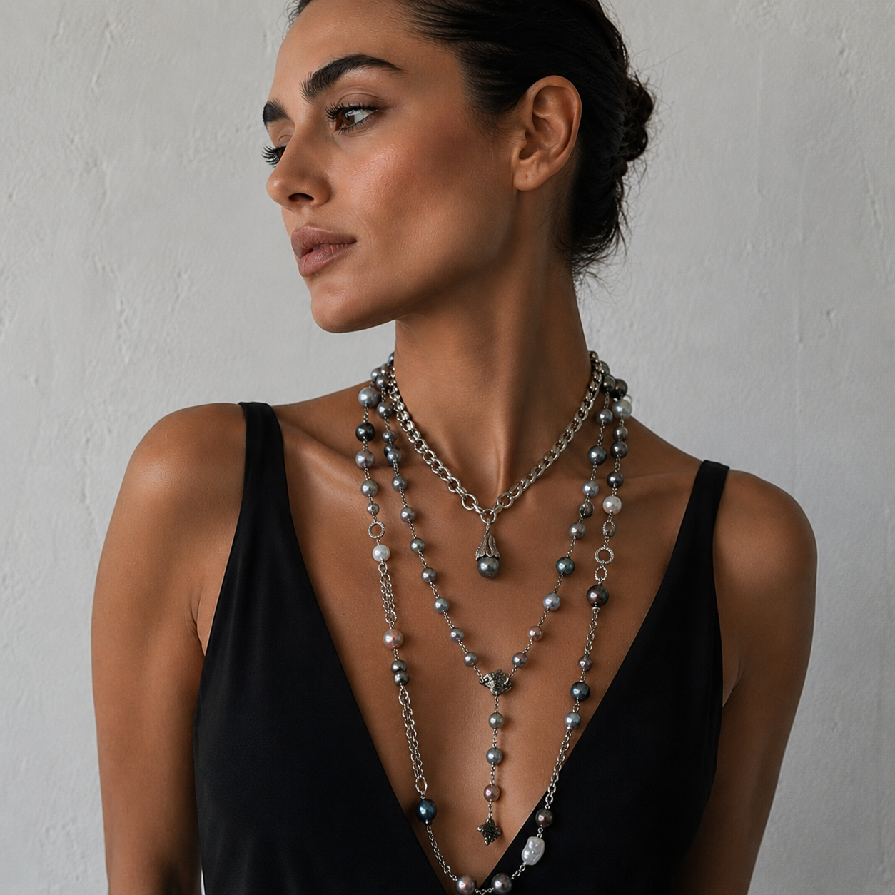 A woman wearing multiple pearl necklaces featuring Tahitian and baroque pearls set in silver-tone chains.