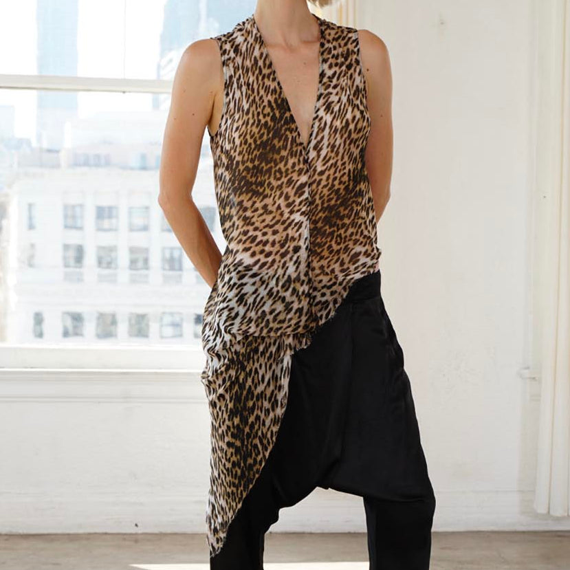 A woman stands in a bright, sunlit studio with large windows, wearing a sleeveless leopard-print top over a black raglan-style harem pant and black espadrille flats.