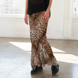 A woman stands in a bright white studio with large arched windows, wearing a black sleeveless top and leopard-print flared pants with black loafers.