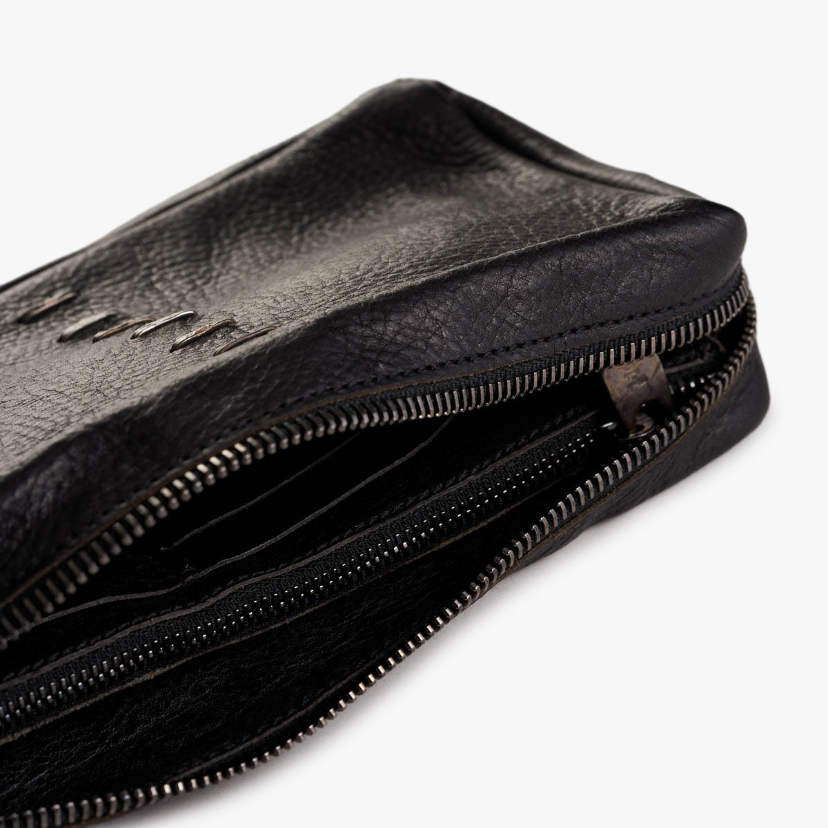 Close-up of a black textured leather zippered bag with a partially unzipped silver metal zipper, shown on a clean white background.
