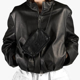 A person wearing a black faux-leather jacket with a front zipper and a matching black crossbody bag with a chain strap, shown against a plain light background.