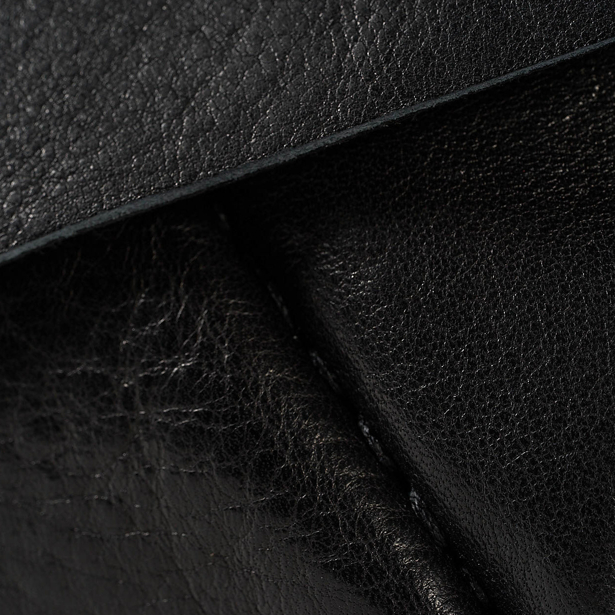 Close-up of black textured leather material with visible grain and stitched edges.