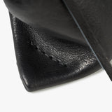 Close-up detail of a black textured leather product, showing a stitched corner and a dark strap against a clean white background.