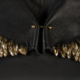 Close-up of a black textured leather clutch featuring a dramatic central fold and rows of sculptural gold-tone metallic shell embellishments along the lower edge.