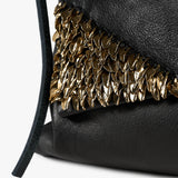 Close-up of a black textured leather bag featuring a prominent metallic gold leaf-patterned trim and a dark strap against a white background.
