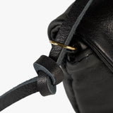 Close-up detail of a black leather bag strap knotted through a gold-tone ring on a white background.