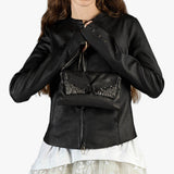 A model wearing a black leather jacket and holding a matching black clutch bag with silver embellishments against a plain white background.