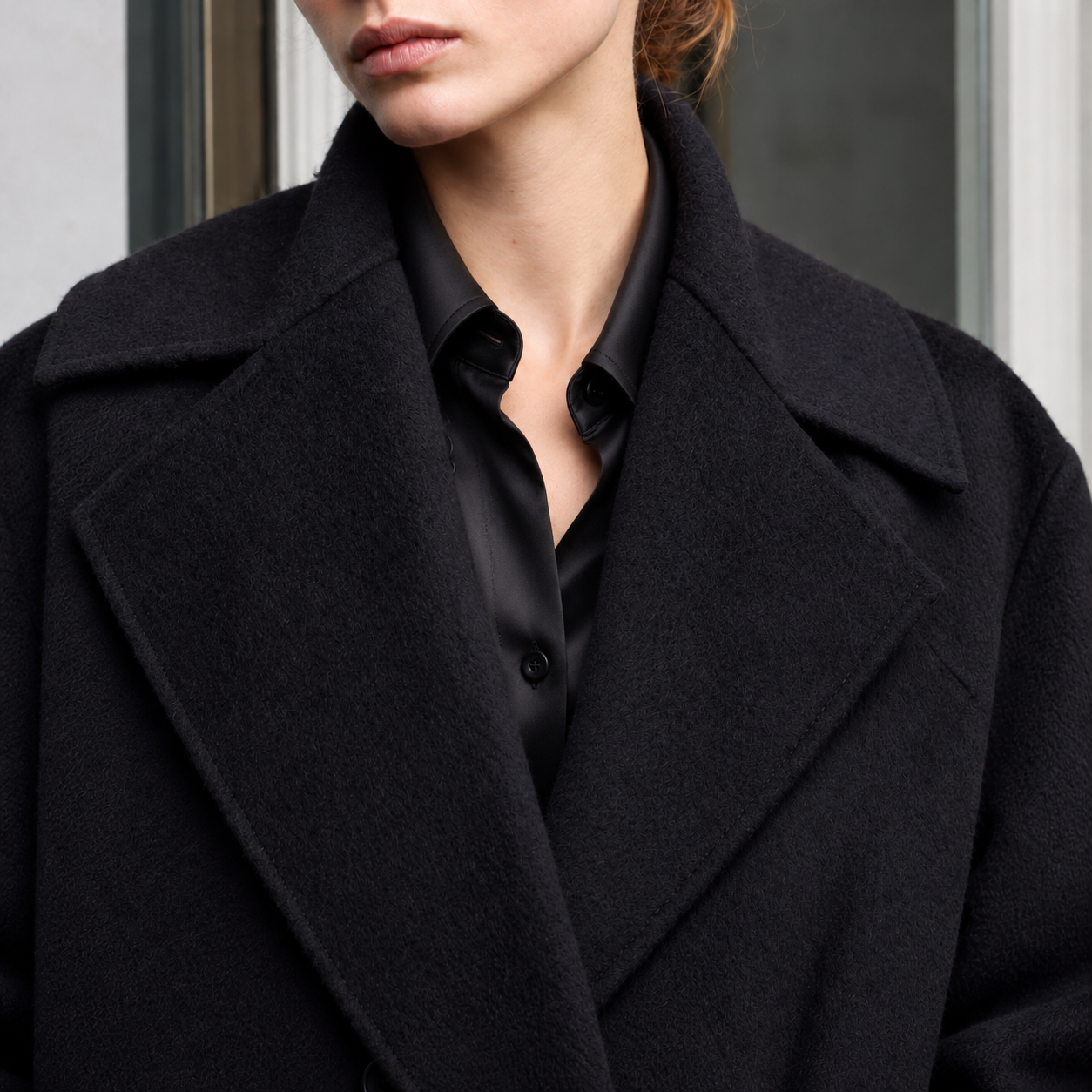 Close-up of a person wearing a black oversized coat over a silk black button-up shirt.