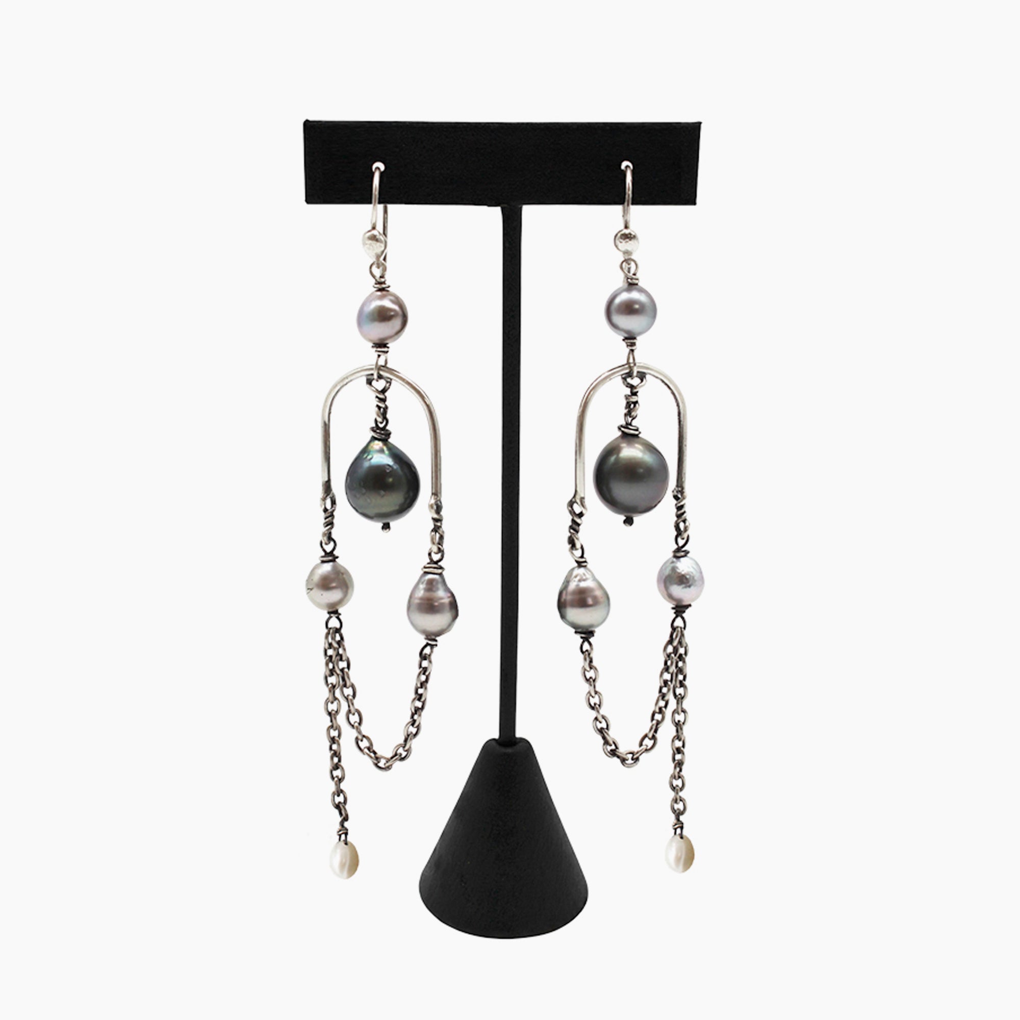A pair of long silver-toned dangle earrings with Tahitian and South Sea pearls, displayed on a black T-stand against a light gray background.
