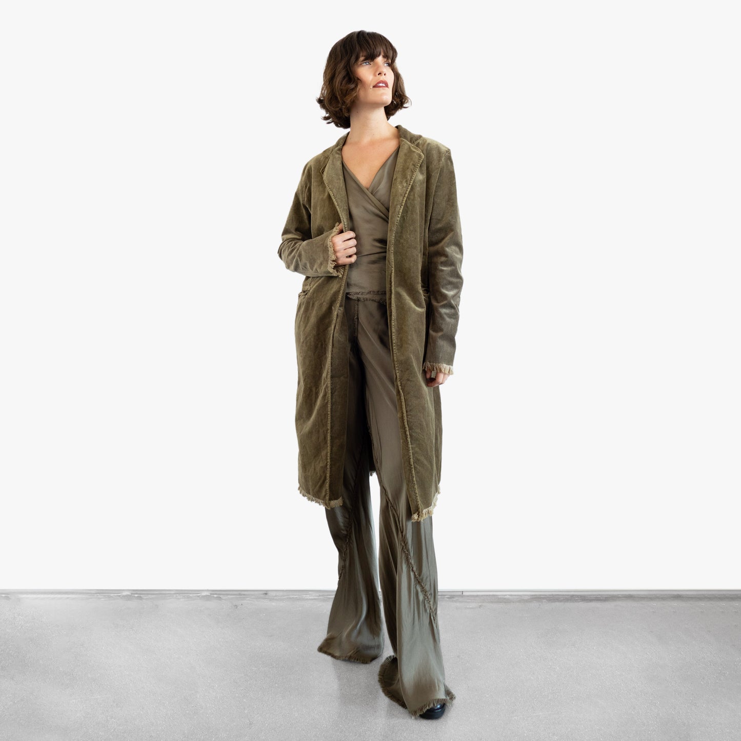 Model wearing a green velvet coat over a green silk wrap top and pants