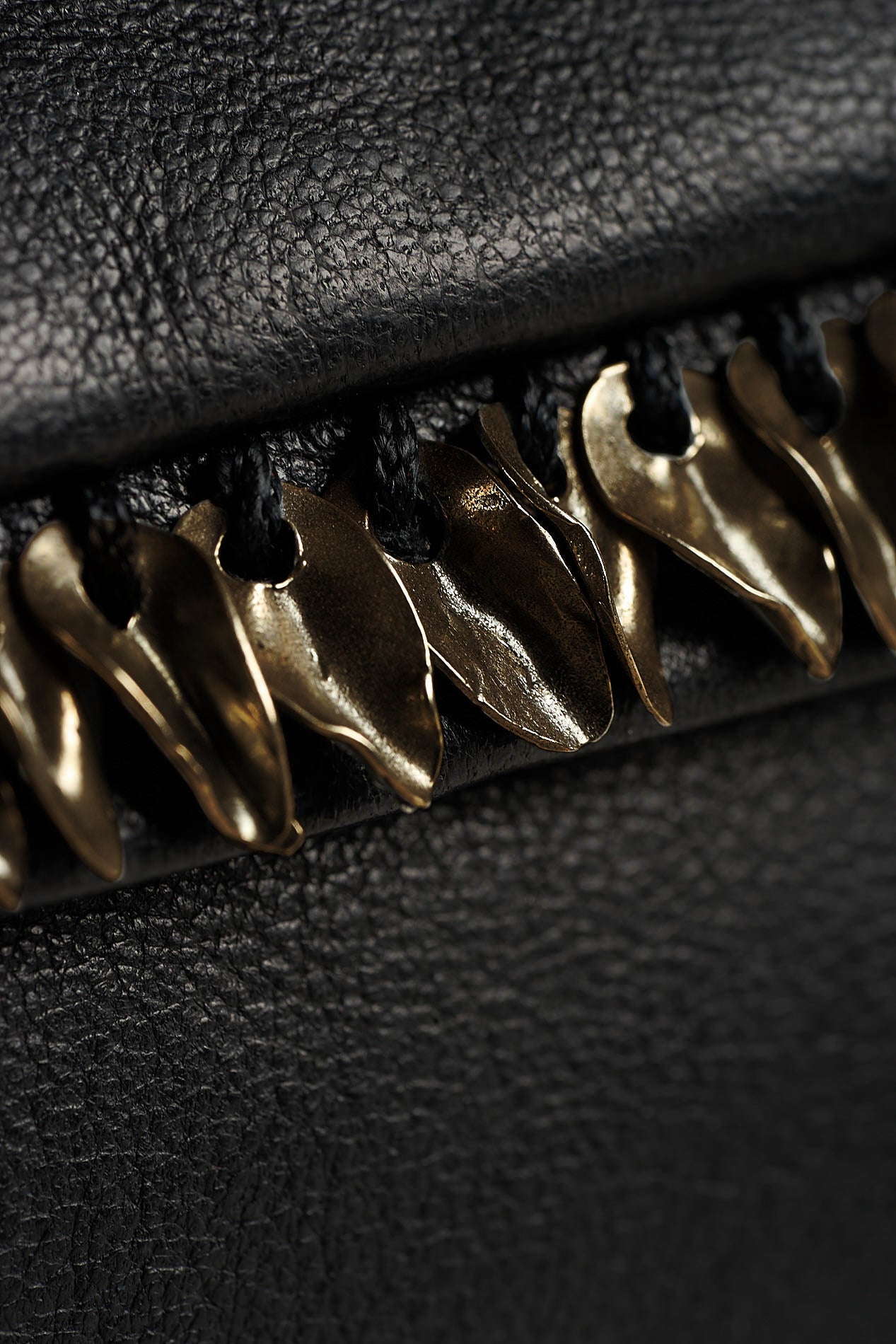 Close-up of a black textured leather item featuring a row of metallic gold bird-shaped hardware accents along the edge.