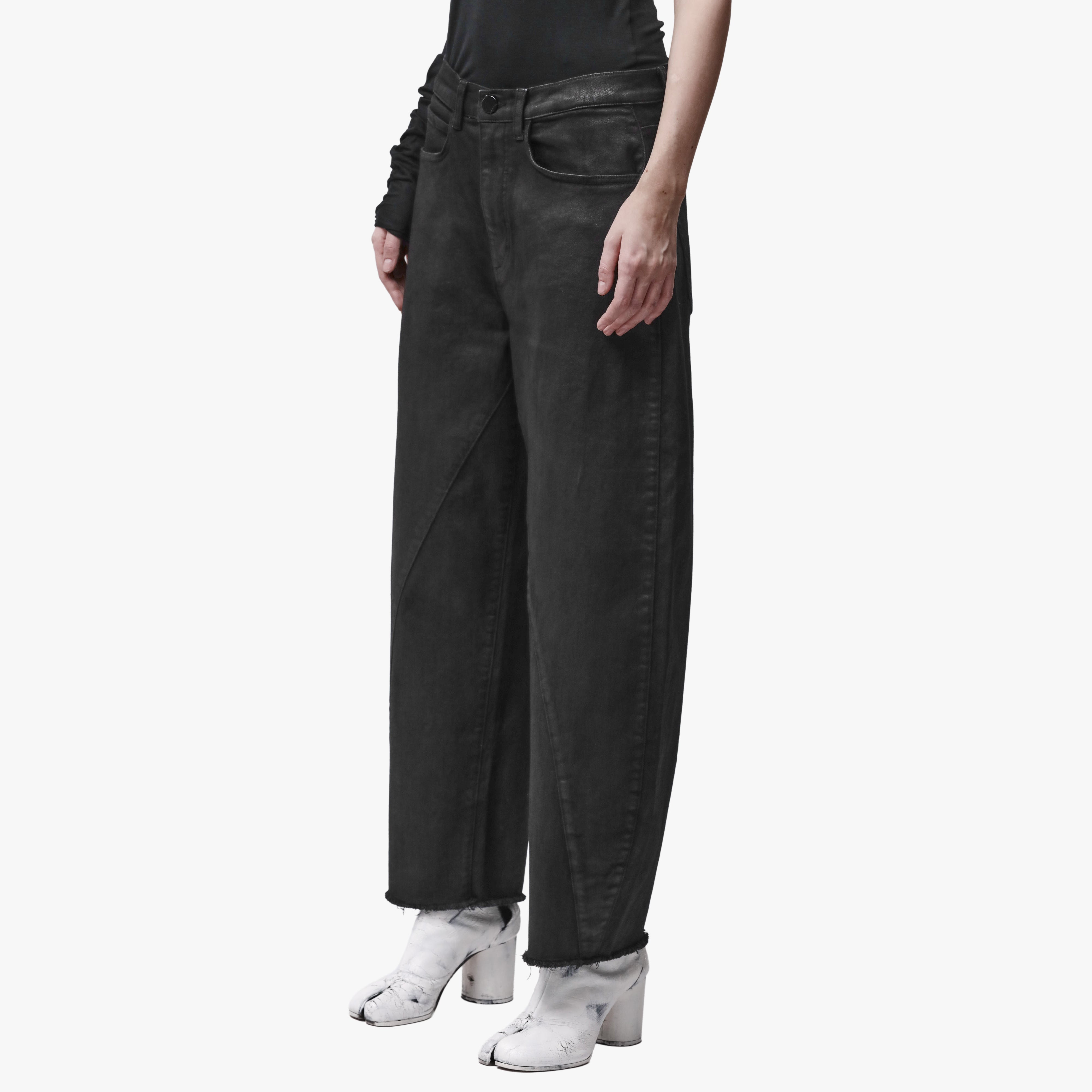A woman wearing black barrel leg jeans facing 3/4 angle