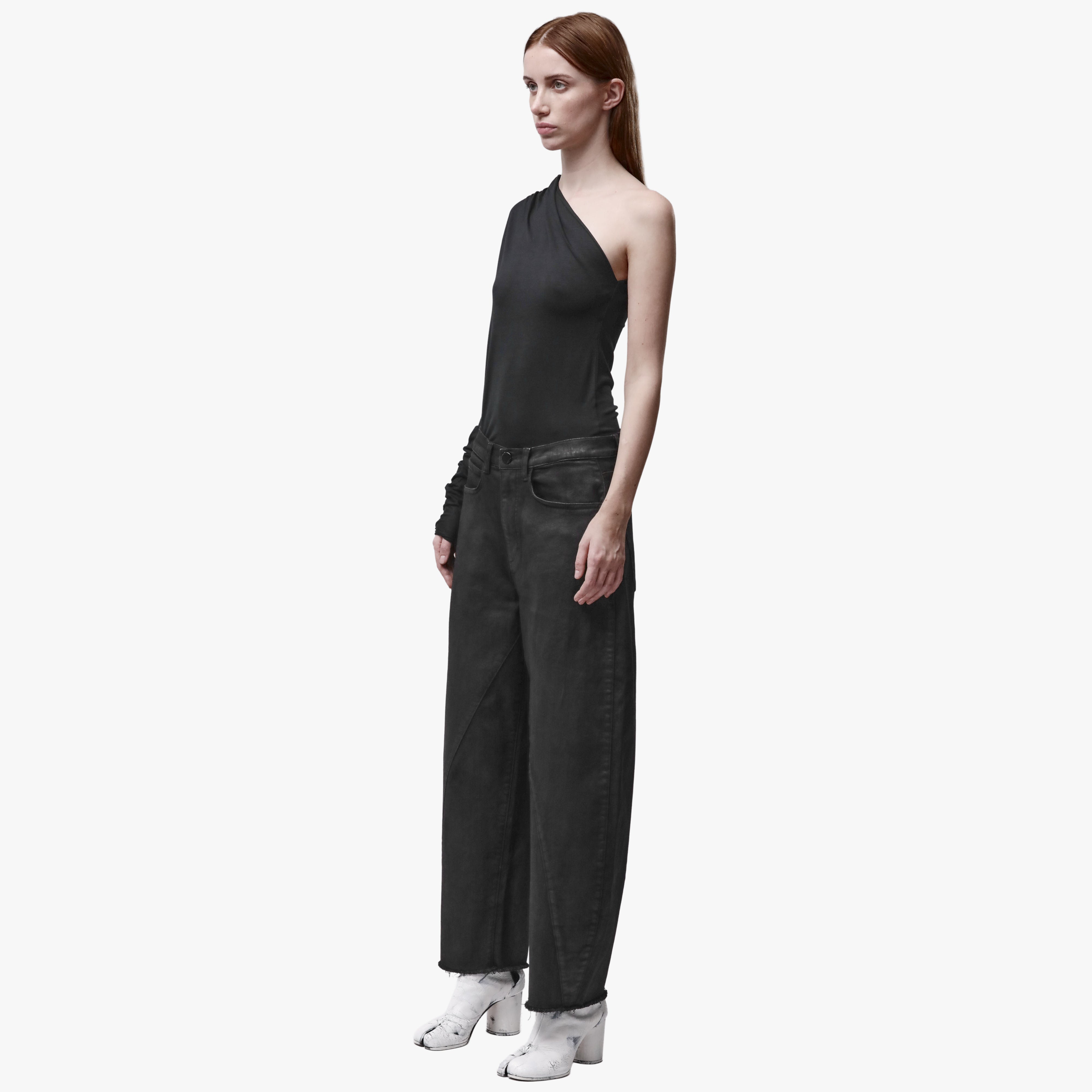 A woman wearing black barrel leg jeans and an asymmetrical top