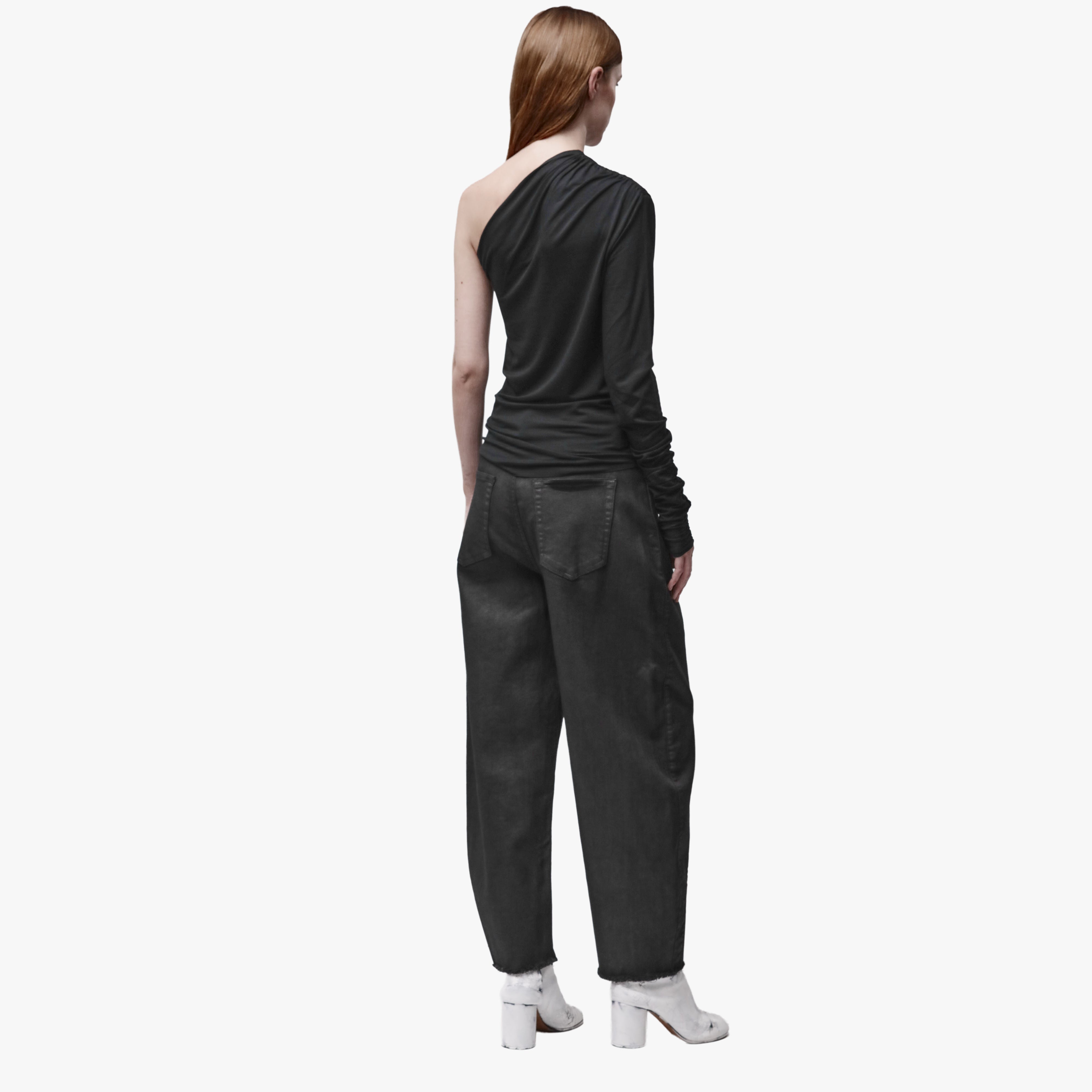 Back view of a woman wearing an asymmetrical black top and black barrel jeans