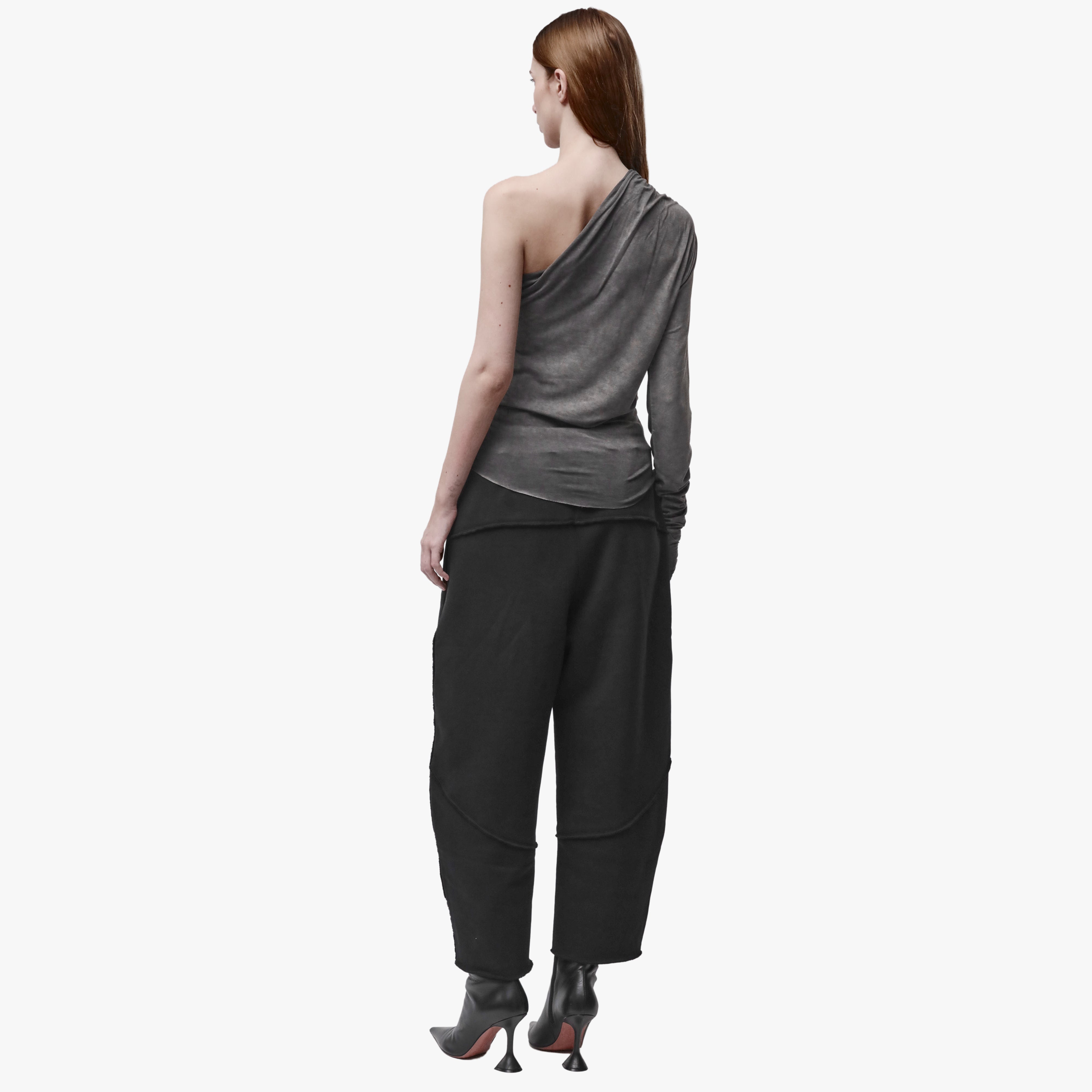 Back view of a woman wearing an asymmetrical grey top and black barrel pants