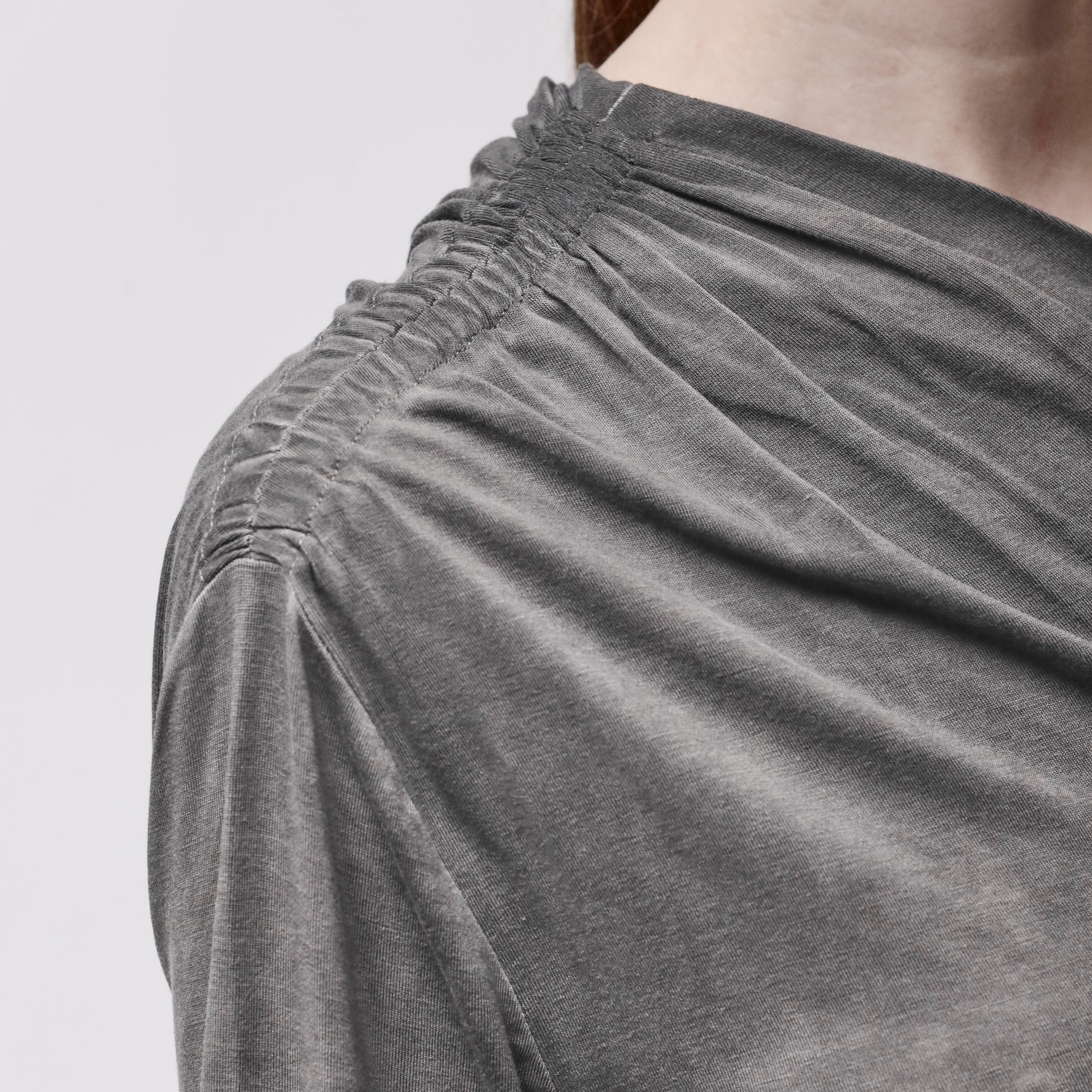 Shoulder detail of a woman wearing an asymmetrical grey top