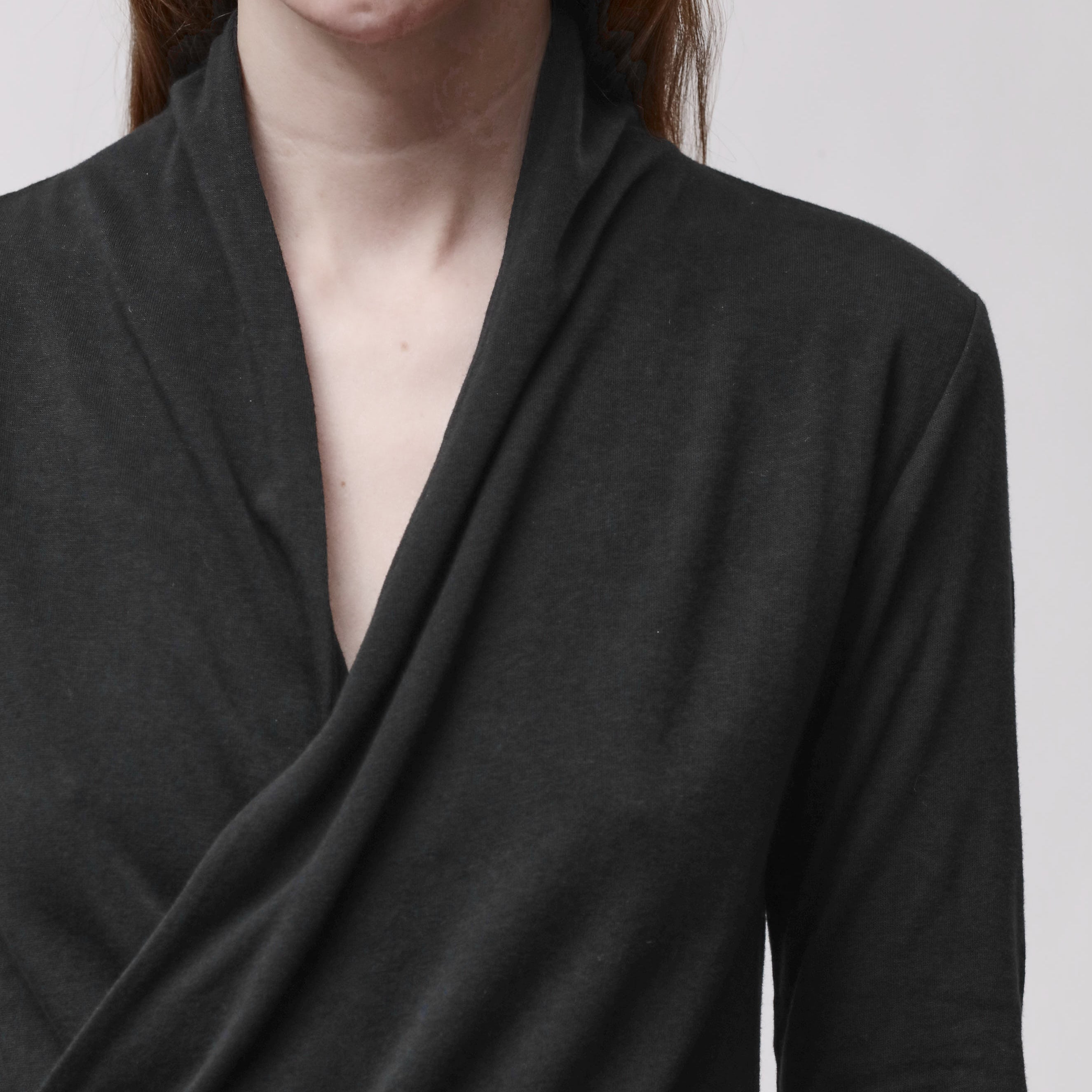 Neckline detail of a woman wearing a long sleeve black wrap top