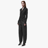 3/4 angle of a woman wearing a long sleeve black wrap top and black barrel jeans
