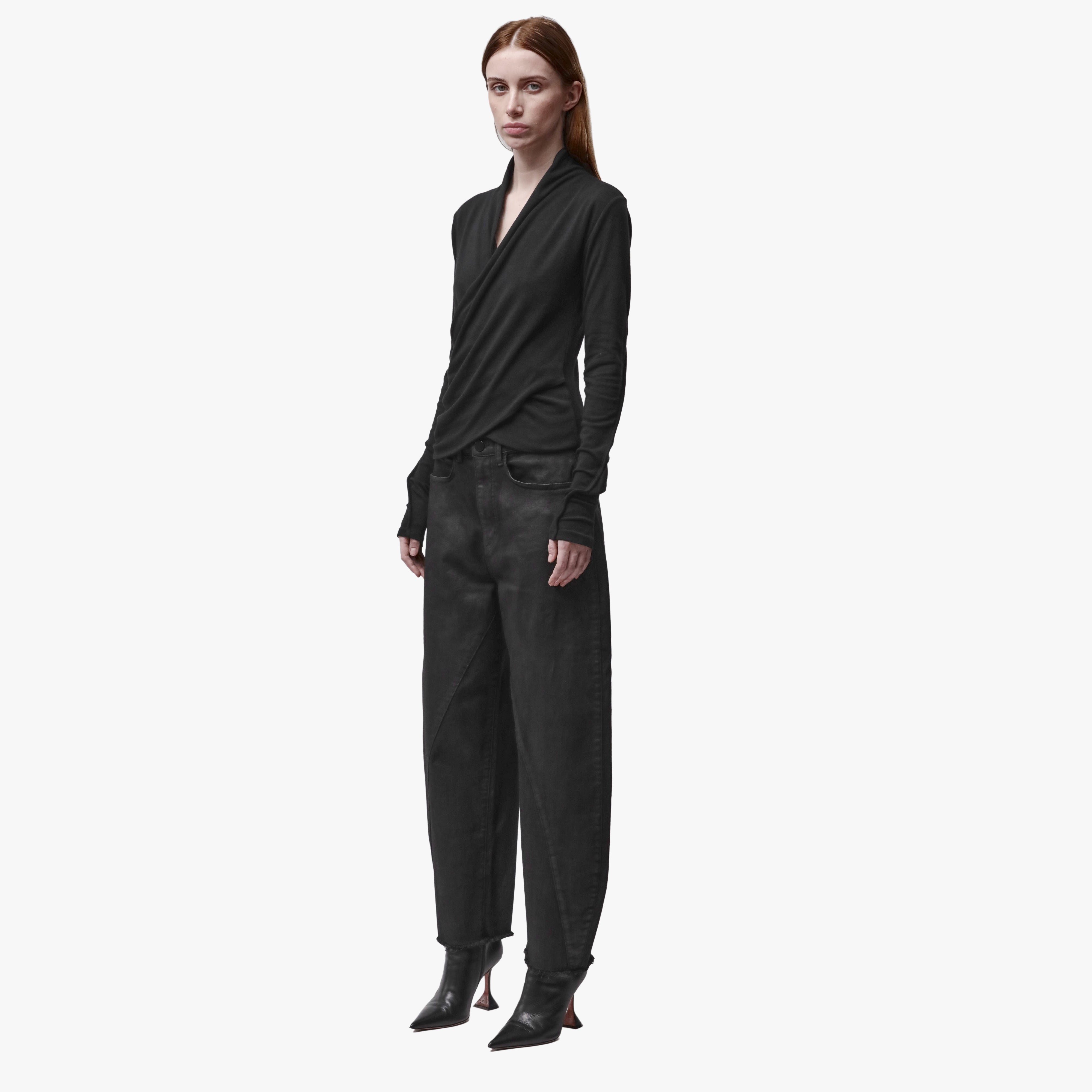 3/4 angle of a woman wearing a long sleeve black wrap top and black barrel jeans
