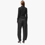 A woman wearing a long sleeve black wrap top and black barrel jeans