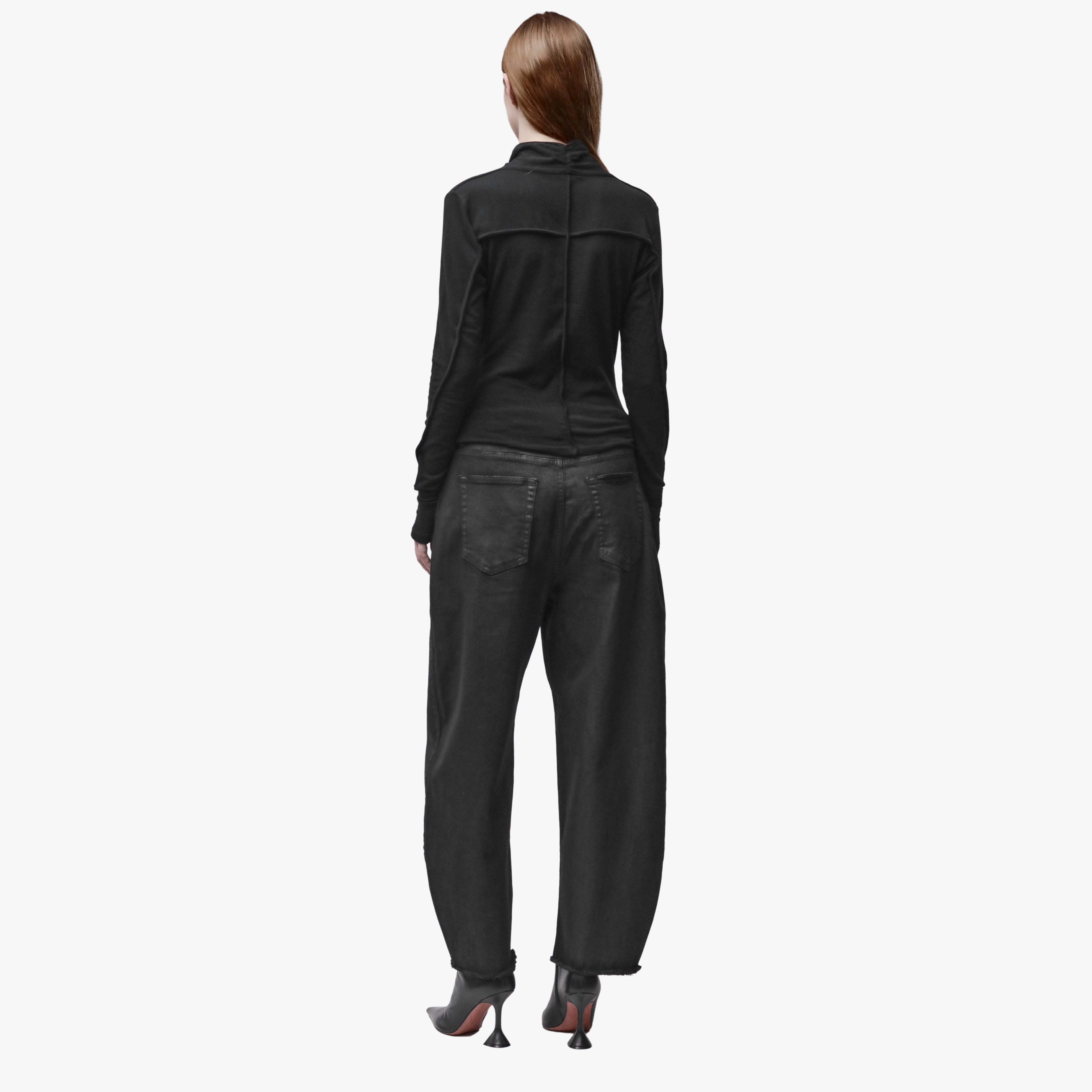 A woman wearing a long sleeve black wrap top and black barrel jeans