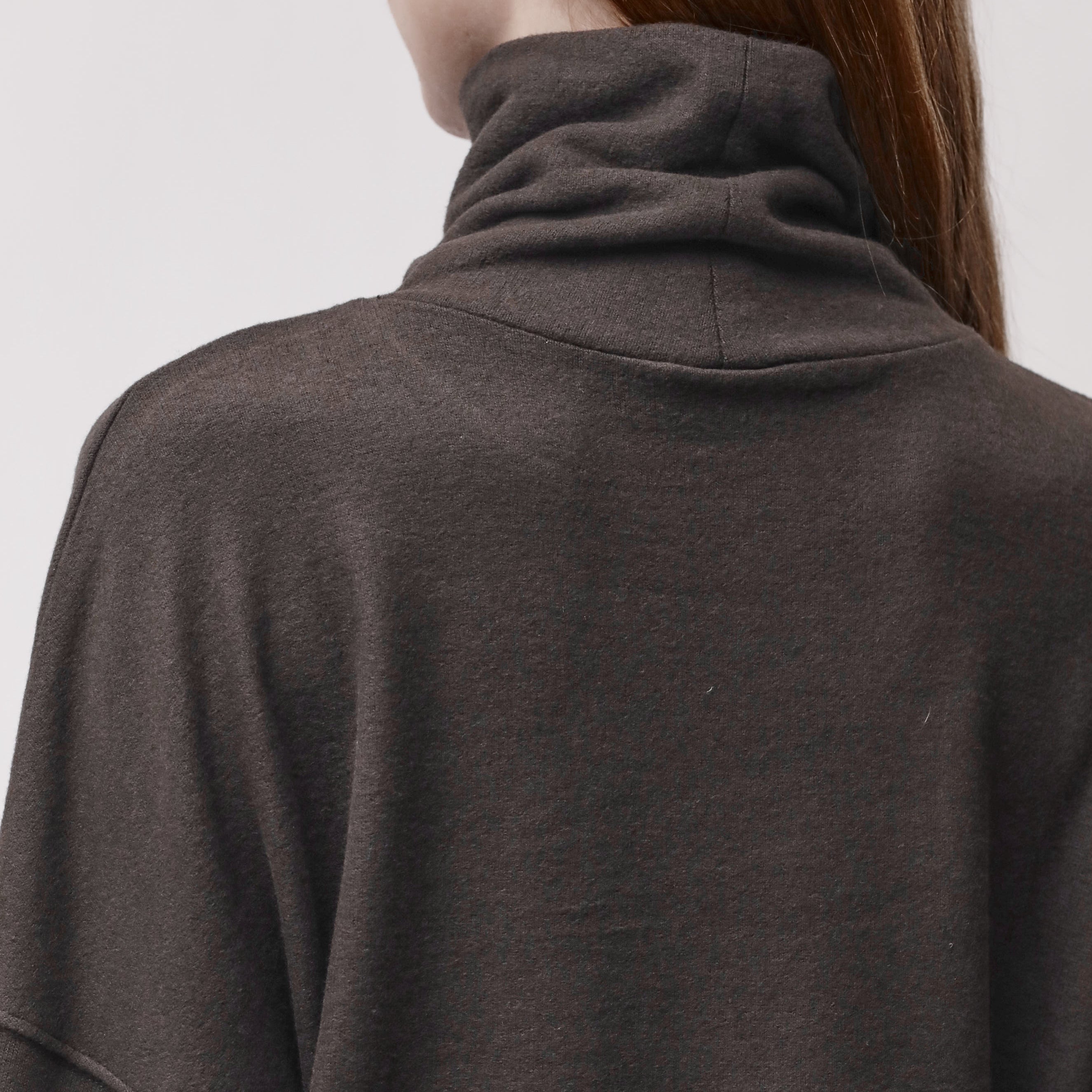Close-up back view of a person wearing a dark brown turtleneck top, showing the neck and upper back against a light gray background.