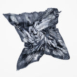 A limited edition hand-painted cashmere and silk scarf in gray, black, and white tones with frayed edges and a silver lamination.