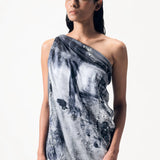 A woman wearing a limited edition hand-painted cashmere and silk scarf in gray, black, and white tones with frayed edges and a silver lamination.