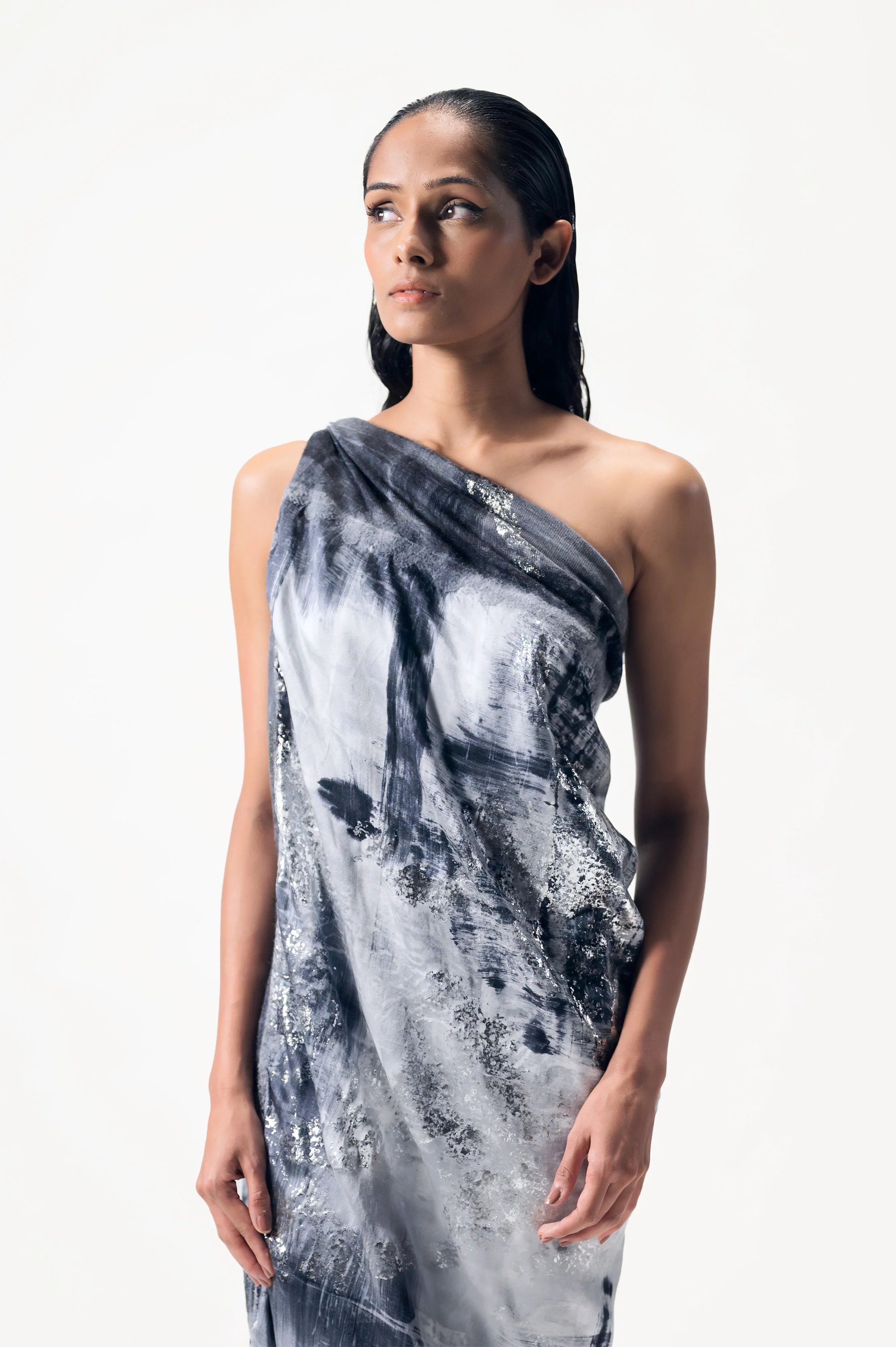 A woman wearing a limited edition hand-painted cashmere and silk scarf in gray, black, and white tones with frayed edges and a silver lamination.