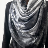 A woman wearing a limited edition hand-painted cashmere and silk scarf in gray, black, and white tones with frayed edges and a silver lamination.