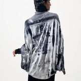 A woman wearing a limited edition hand-painted cashmere and silk scarf in gray, black, and white tones with frayed edges and a silver lamination.